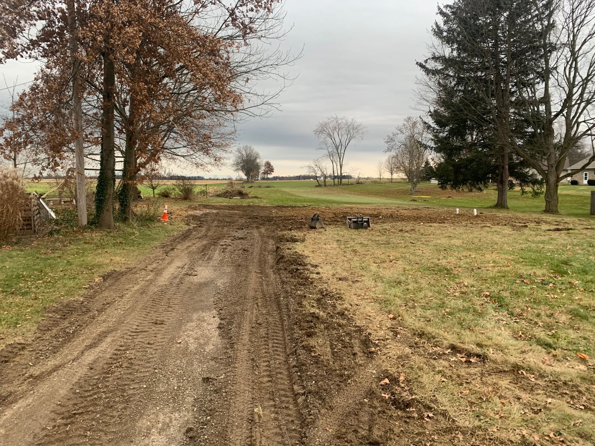 Muddy dirt path in field with trees and overcast sky.