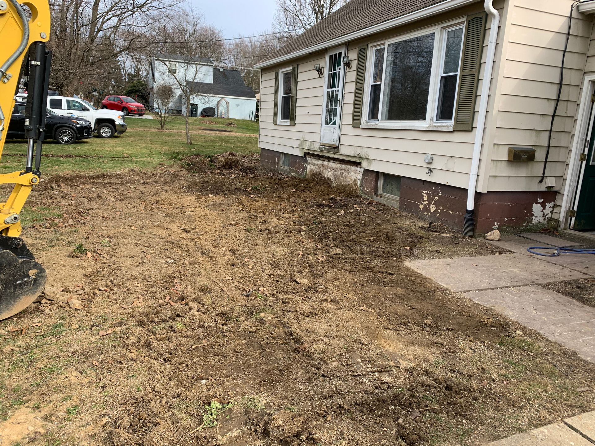 Dirt patch in front of a house, possibly prepared for landscaping. An excavator is visible to the left.