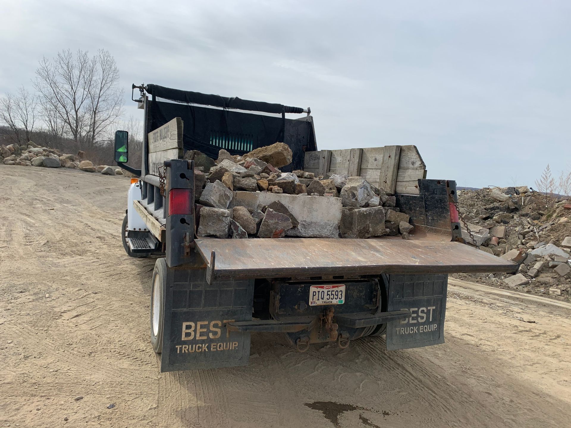 A white truck bed filled with rocks and concrete debris, parked on a gravel lot under an overcast sky.