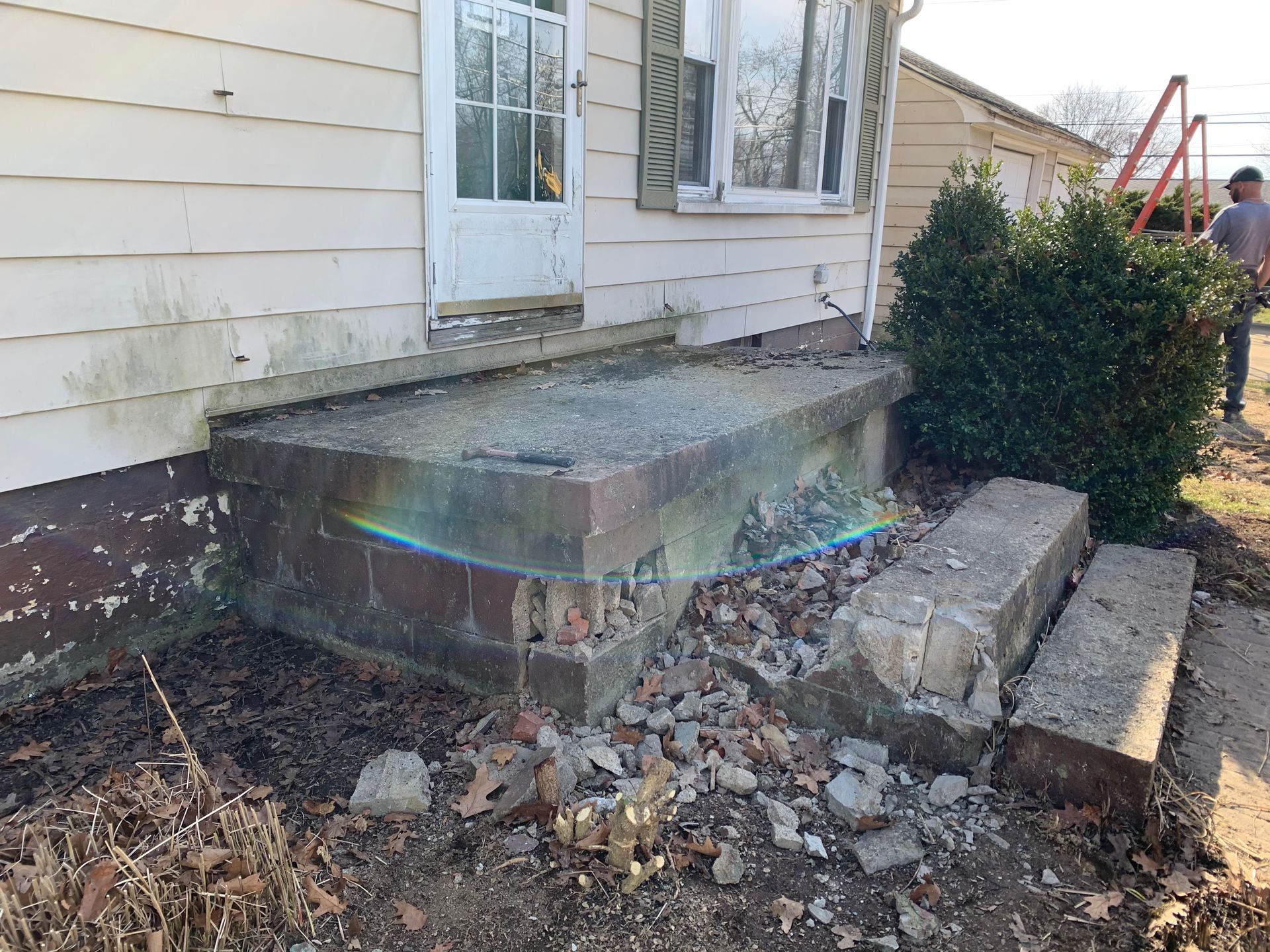 Damaged concrete porch and steps of a house; brick facing crumbling, debris on ground.