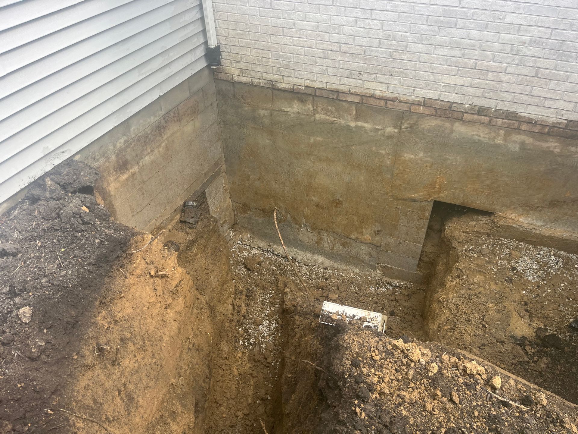 Foundation excavation with dirt trench, concrete wall, and house siding.