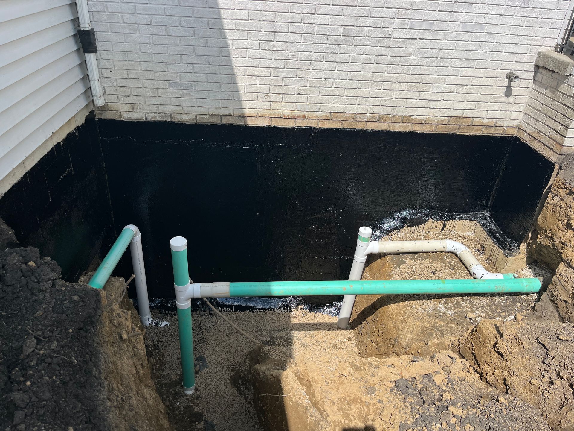 Excavation with black waterproof coating on a foundation wall and PVC pipes for drainage.