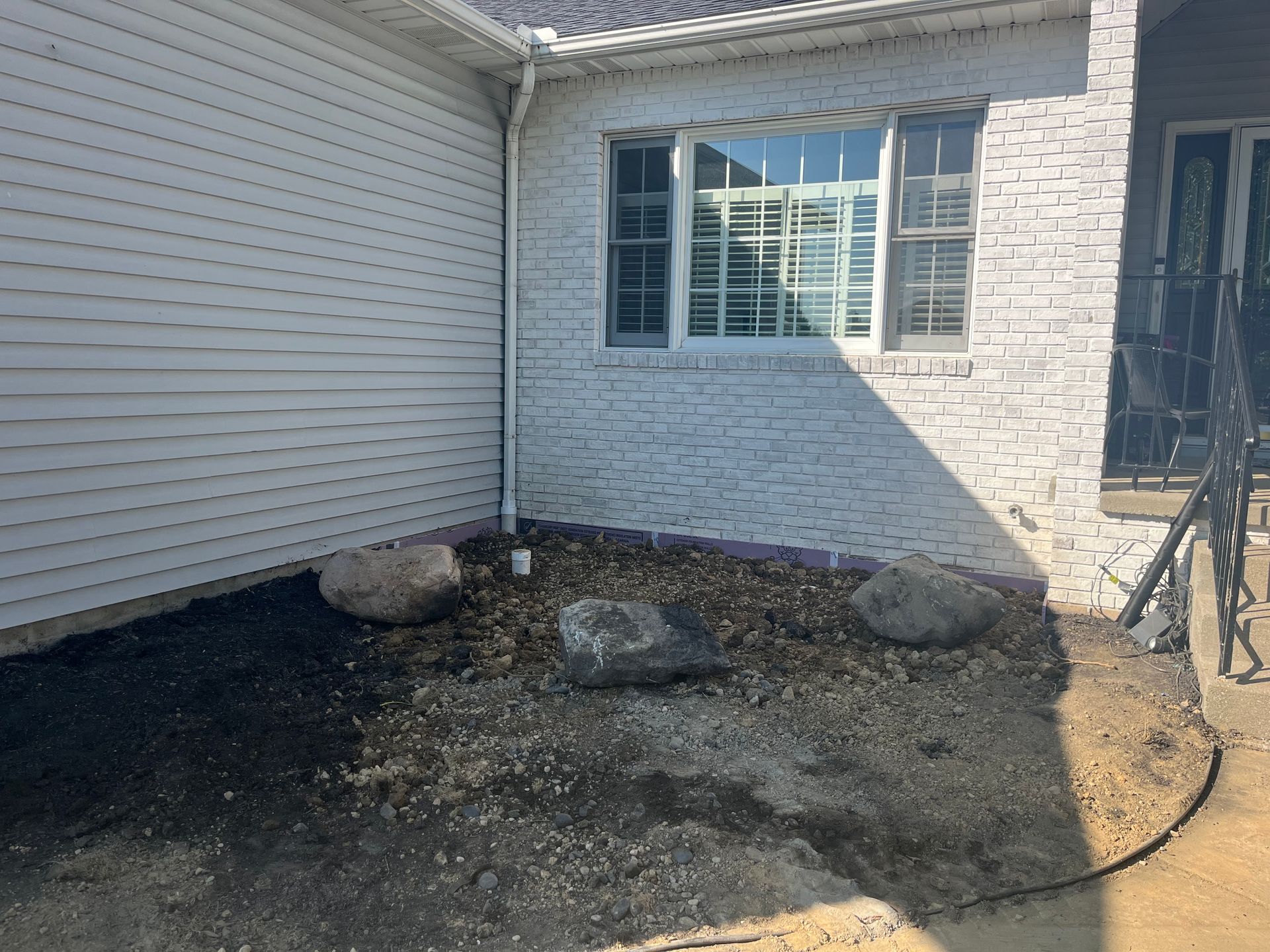 Exterior view of a house with a gravel bed, large rocks, and a white brick wall near a window.