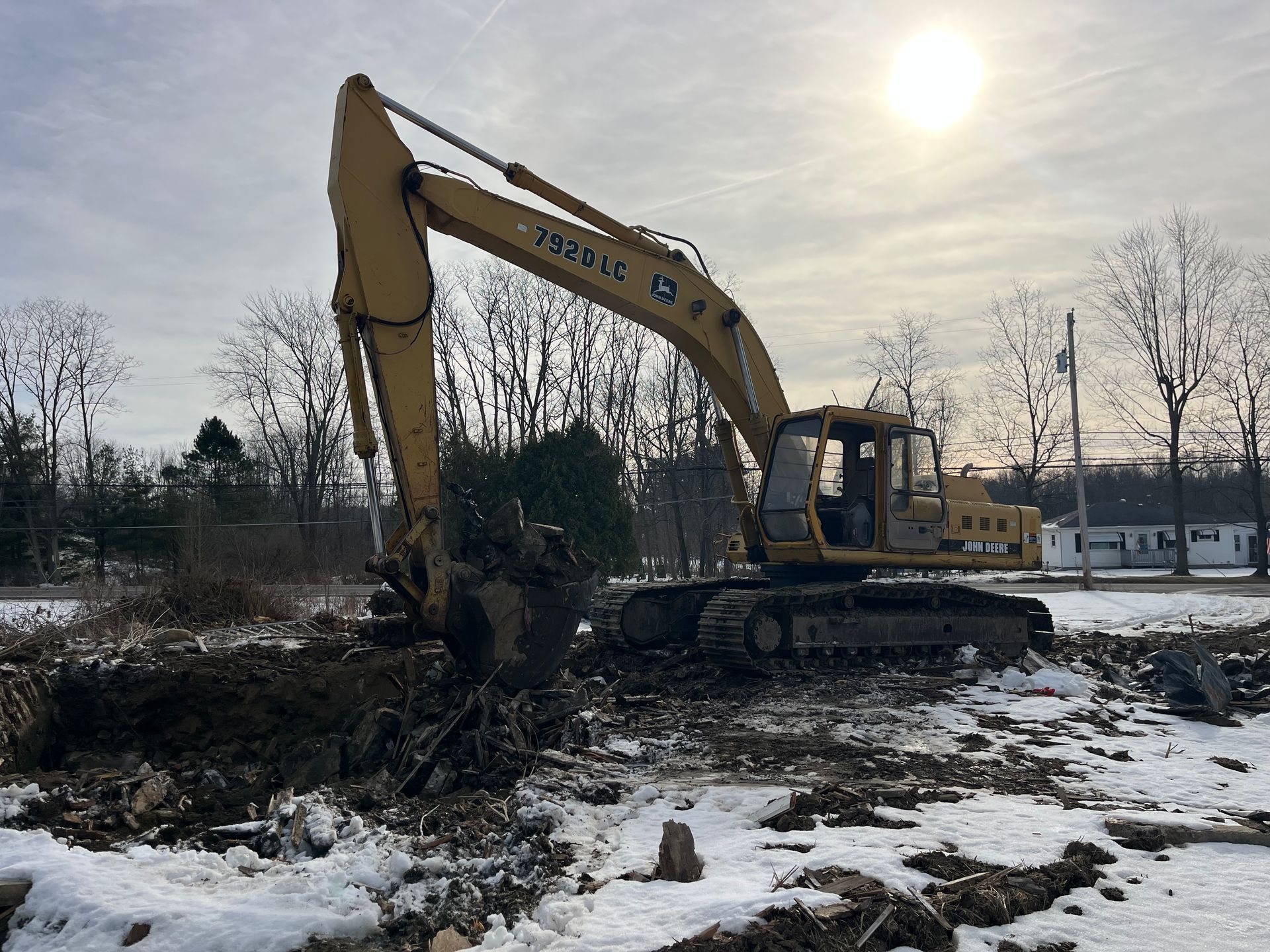 Yellow excavator, digging in snow-covered dirt, under a sunny sky.