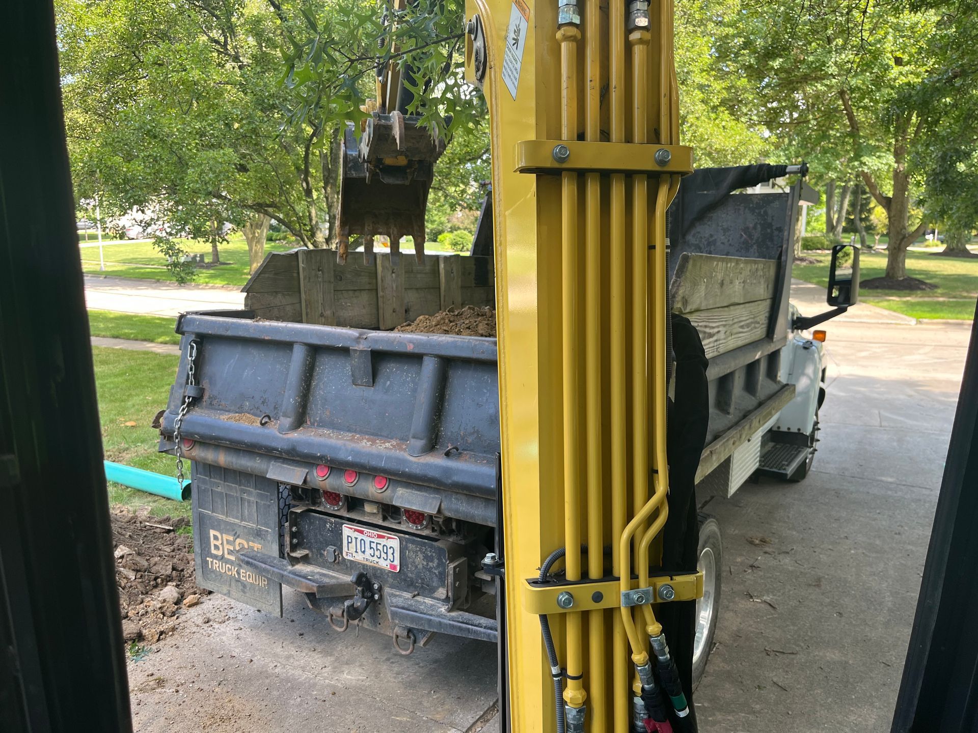 Yellow excavator loading dirt into a dump truck on a driveway.