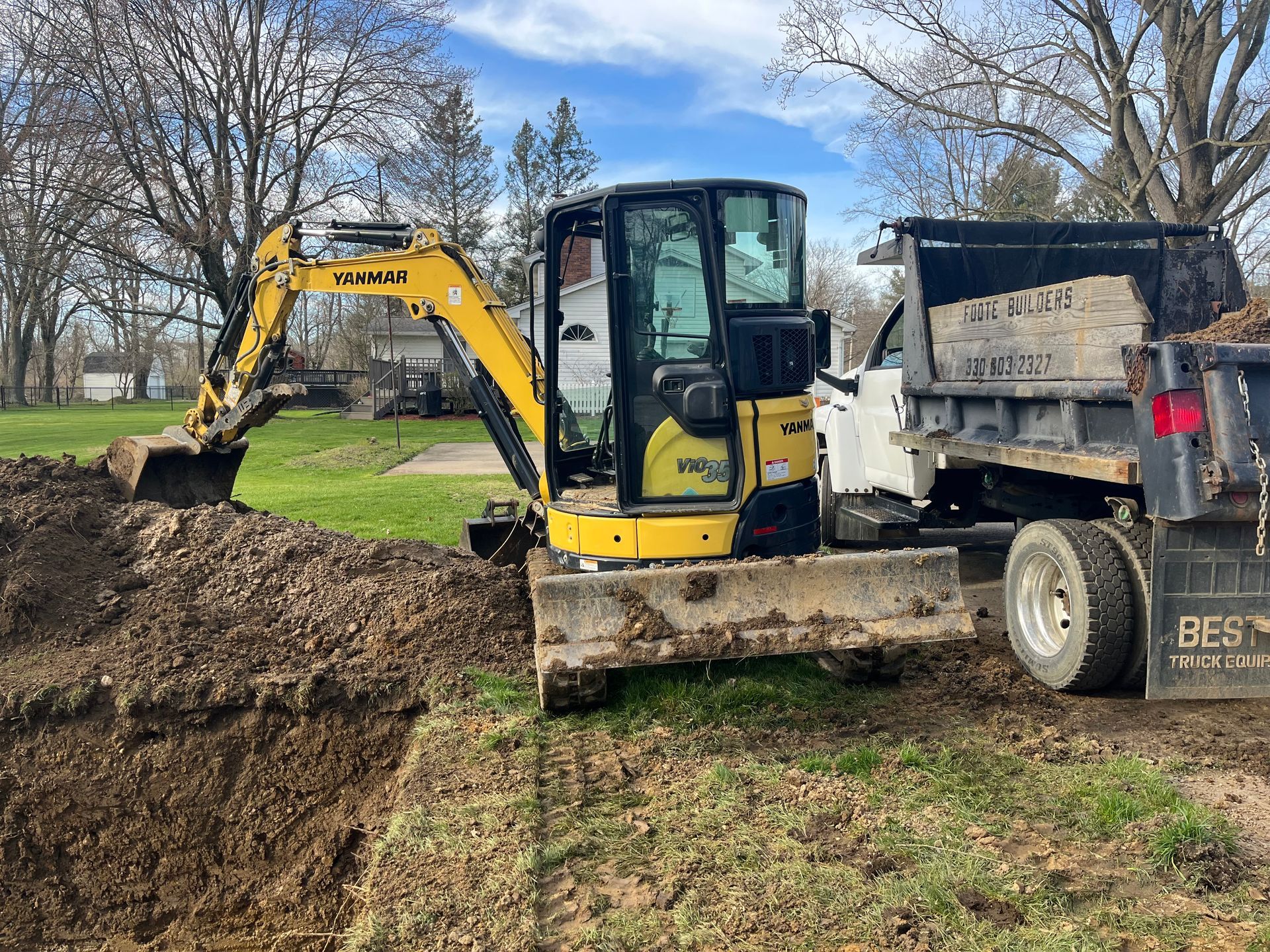 Yellow excavator loading dirt into a white truck bed on a grassy area.