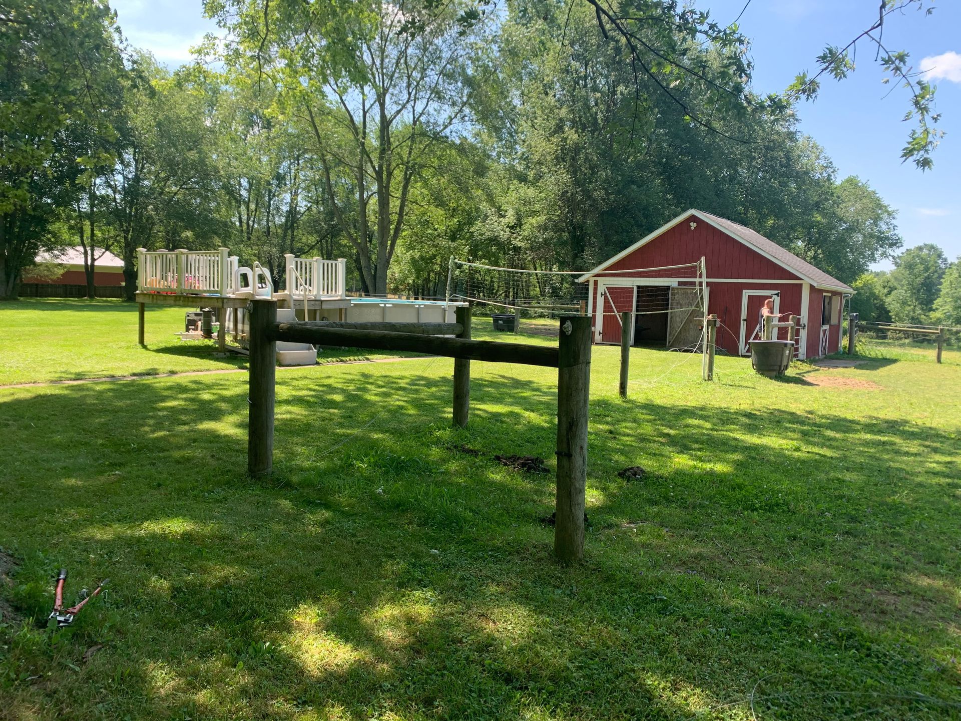 Green grassy yard with a red barn in the background and a trailer with equipment.