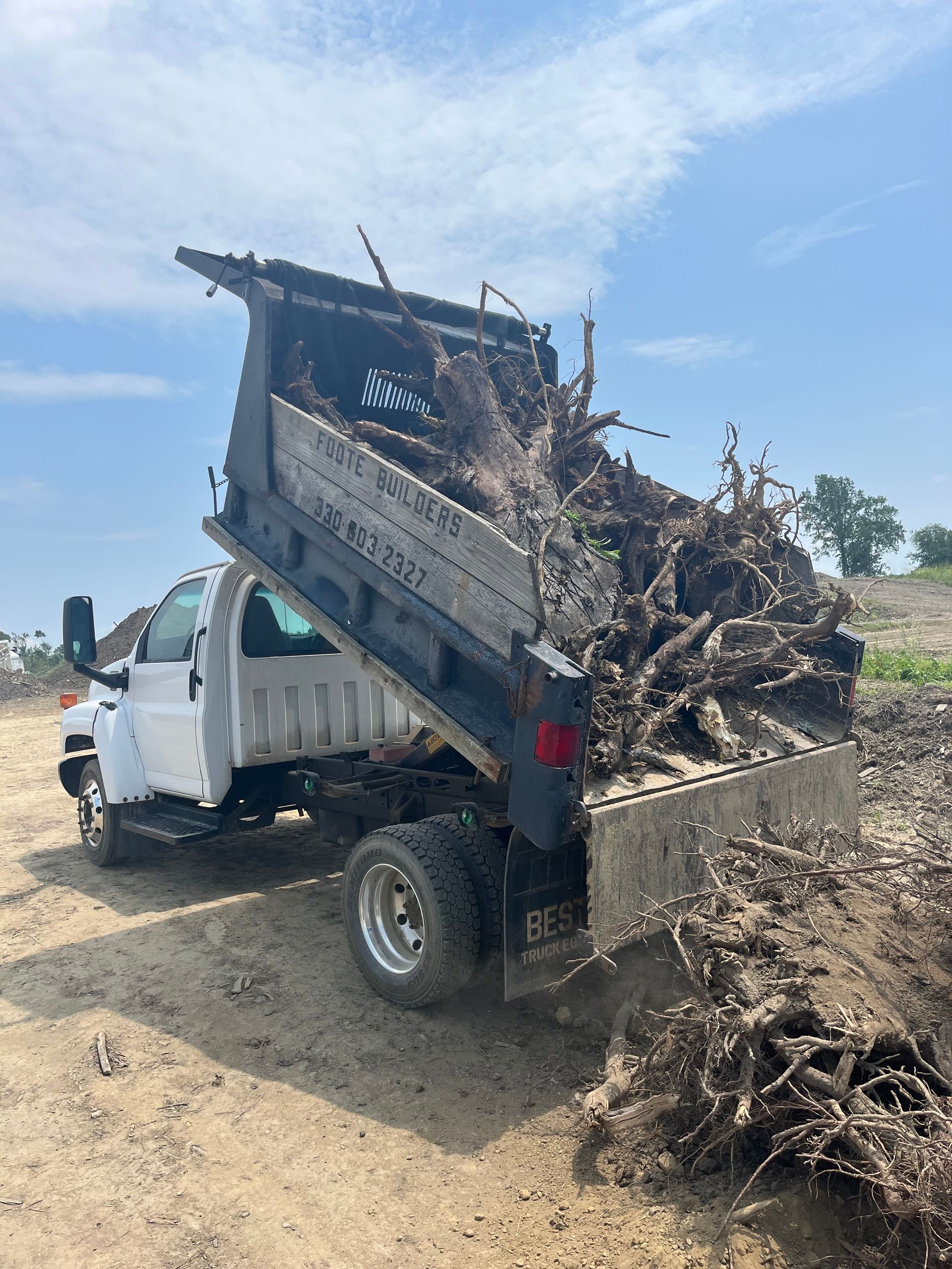 White dump truck unloading mulch on a dirt lot under a blue sky.