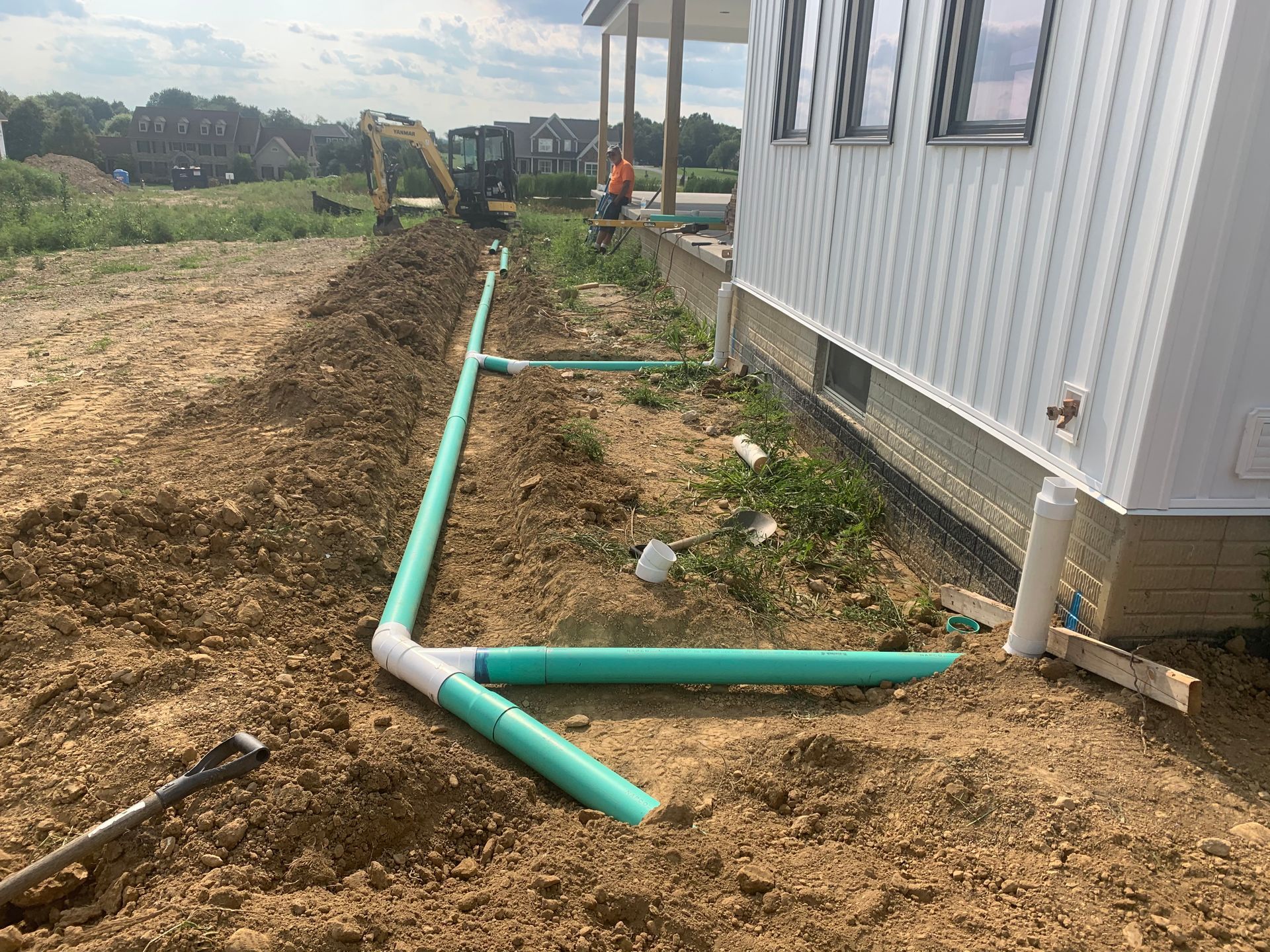 Green PVC pipes installed in a trench next to a white building. Construction site.