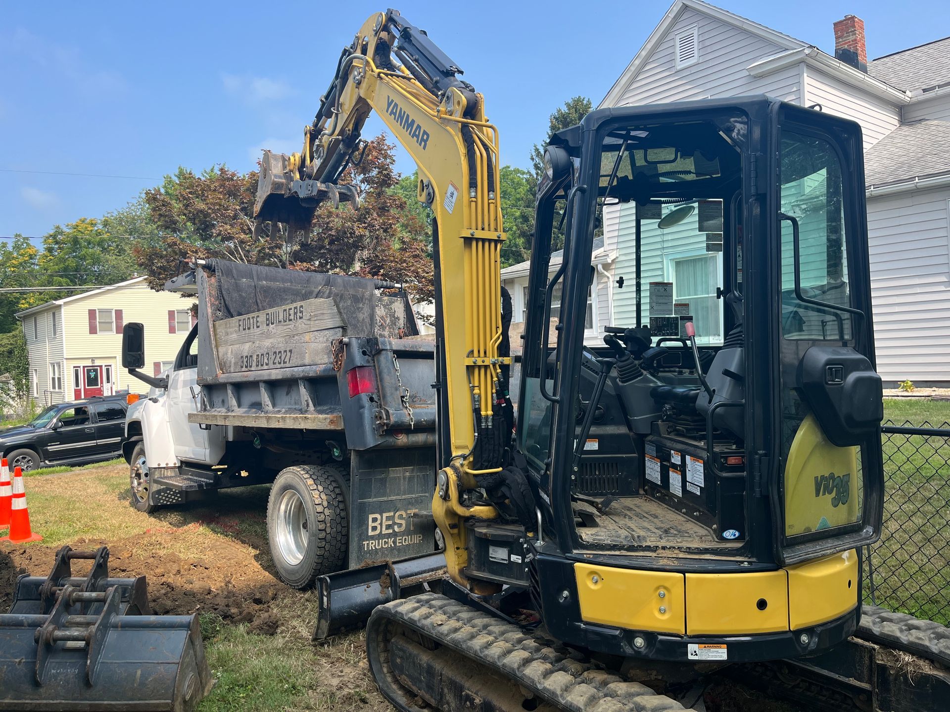 Yellow excavator loading a dump truck with dirt on a construction site next to a house under a blue sky.