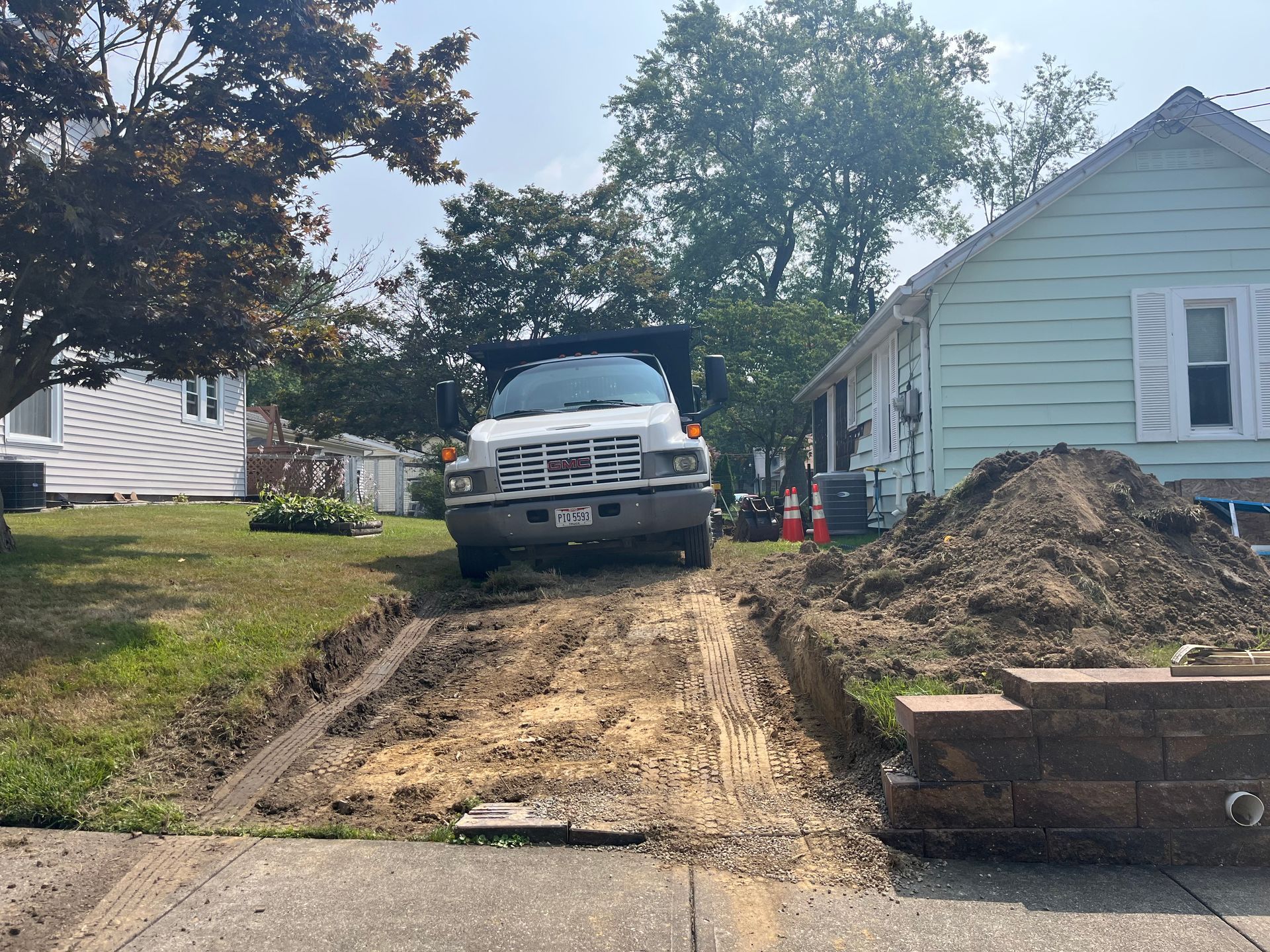 White truck parked on a dirt ramp beside a house under construction; dirt pile, brick wall, and trench visible.