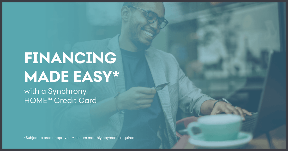 Man smiling, using laptop and holding credit card; financing made easy with Synchrony HOME credit card.