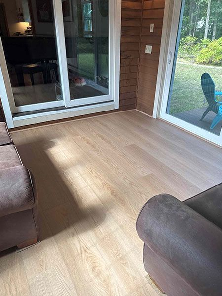 A light-colored wood floor in a sunroom with glass sliding doors and brown furniture.