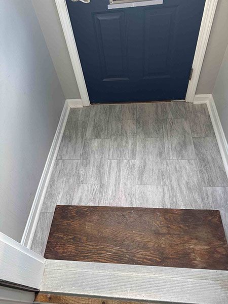 Hallway with grey tile flooring, dark blue door, white trim, and a brown doormat.