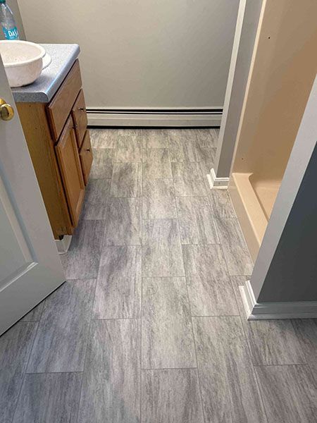 Bathroom with gray wood-look flooring, wooden vanity, and shower entrance.