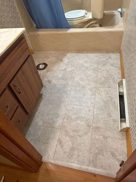 Bathroom with a vanity, toilet, and bathtub. Beige tile floor and tan walls.
