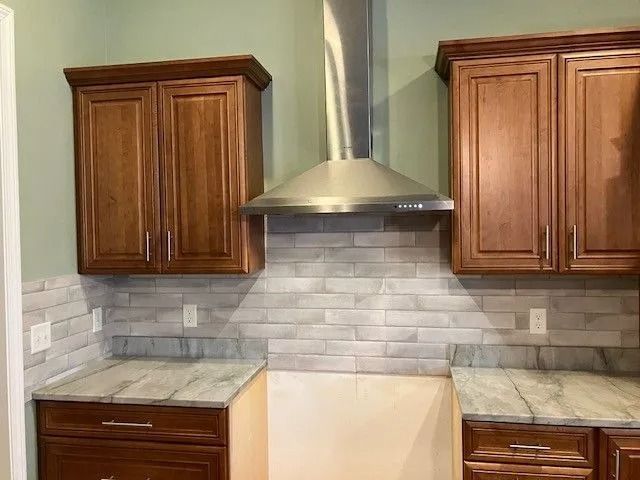 Kitchen with wood cabinets, gray countertops, white brick backsplash, and stainless steel range hood.