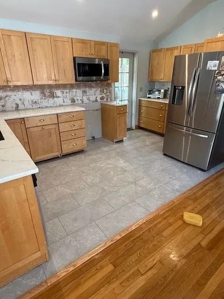 Kitchen with light wood cabinets, stainless steel appliances, gray tile floor, and wood floor.