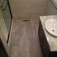 Bathroom with gray tile floor, shower with glass door, and vanity with a white sink.