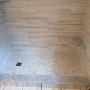 Shower with light-colored stone tiling; has a drain and curved corner design.