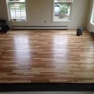 Hardwood floor in a room with two windows, light brown and shiny.