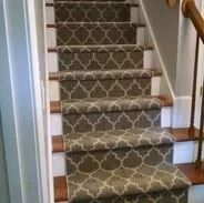 Staircase with patterned gray carpet runner and wooden stairs. White risers and wooden railing on the right.