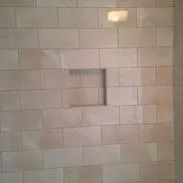 Beige tiled shower wall with recessed square shelf.