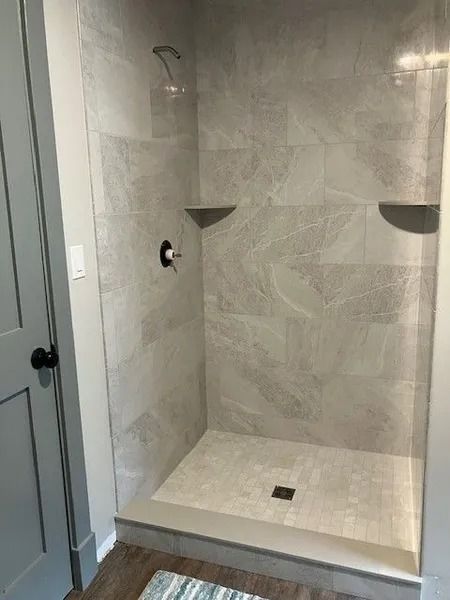 Gray tiled shower with two built-in shelves, a showerhead, and a dark faucet.