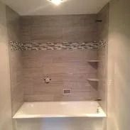 Bathtub with gray tiled walls, mosaic accent, and built-in shelves.