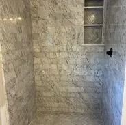 Shower with marble-like gray tile and built-in shelf, with black showerhead.