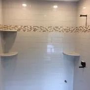 White tiled shower with two corner shelves and a decorative mosaic band.