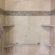 Shower with beige tiled walls, mosaic border, shelves, grab bar.