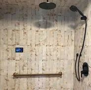 Shower with black fixtures, handheld shower head, and a horizontal grab bar on textured wall.