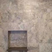 Shower wall with a built-in shelf, tiled with large, mottled gray-beige tiles.