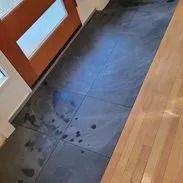 Dark tiled floor, possibly wet, next to wooden floor and door.