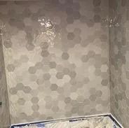 Gray hexagon tile wall in a shower with some reflection near the top.