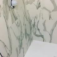 White marble tiled bathroom with silver veining, shower head.