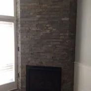 Fireplace with dark stone facade, black hearth. Window on left. White trim.