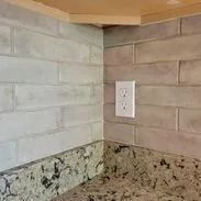 Corner of a kitchen with light brick-style backsplash, granite countertop, and electrical outlet.