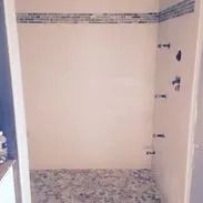 Walk-in shower with mosaic floor and tiled walls, horizontal band of accent tiles near the top.