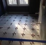 Tiles being laid on a floor with leveling spacers, in a room with a window.
