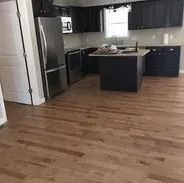 A kitchen with dark cabinets, stainless steel appliances, and light wood floors.
