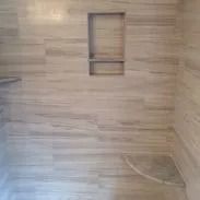 Beige-tiled shower interior with a built-in shelf and a curved base, horizontal tile pattern.
