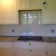 Cream-colored kitchen cabinets with a tiled backsplash and cooktop in a kitchen.