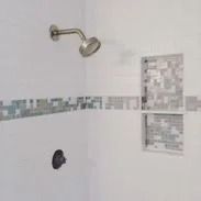 Shower with white tiles, a decorative mosaic tile strip, and a recessed shelf.