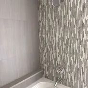 Bathroom with grey and white patterned tile backsplash, shower fixtures, and a bathtub.