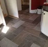 Herringbone pattern tile floor in a kitchen with a doorway and white cabinets.