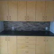 Kitchen with light wood cabinets, dark countertop, and mosaic tile backsplash.