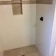 White tiled shower with a built-in shelf and dark fixtures.