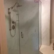 Glass shower enclosure with marble-look walls and silver shower fixtures.